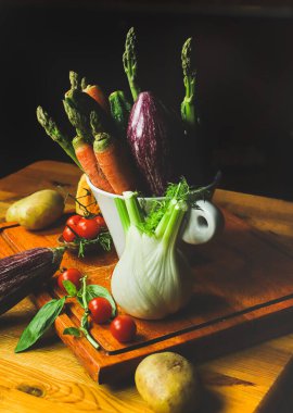 Karanlık mutfakta, ahşap masada taze sebzeler.