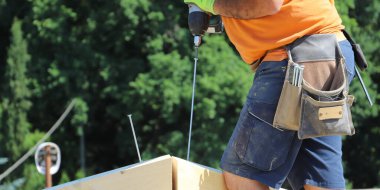 Ellerinde testereyle koruyucu kasklı ve eldivenli bir işçi.