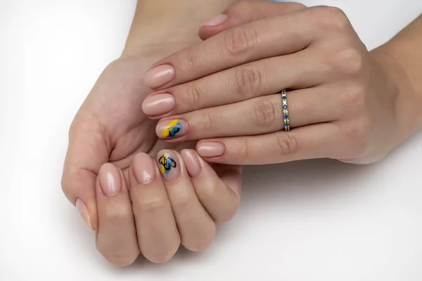 Natural beige manicure on short oval nails. Ukrainian symbols. Yellow blue drawing. Heart drawing.