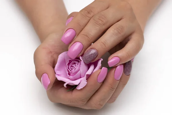 Gently pink manicure with shimmer with a rose in the palm of your hand on long square nails close-up on a white background