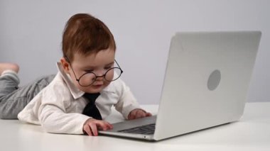 Gözlüklü ve takım elbiseli şirin bebek dizüstü bilgisayarla çalışıyor.