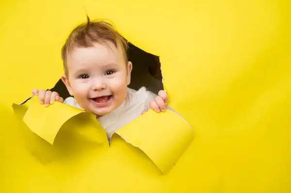 Kağıt sarısı arka planda bir delikten çıkan beyaz bir bebek.
