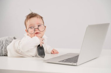 Gözlüklü ve takım elbiseli şirin bebek dizüstü bilgisayarla çalışıyor.