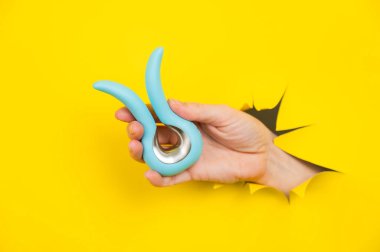 Sarı kağıt arkaplanından sarkan mavi vibratörü tutan kadın.