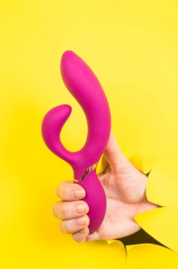 Sarı kağıt arka plandan sarkan mor vibratörlü kadın eli. Boşluğu kopyala
