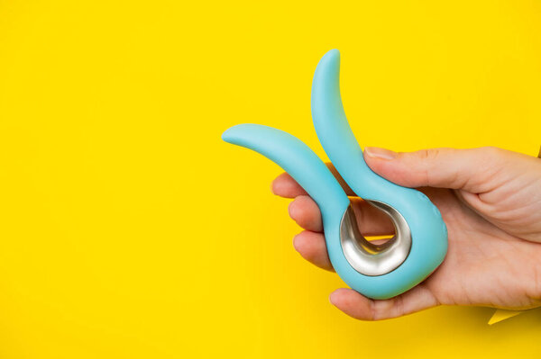 Женская рука держит синий вибратор торчащий из желтого бумажного фона