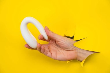 Beyaz vibratör tutan kadın el sarı kağıt arka planda sıkışmış.