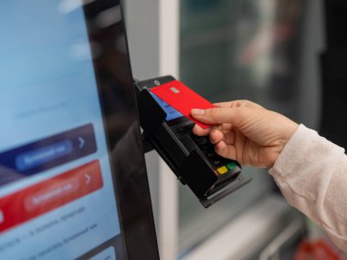 Bu resim, bir otomatik ödeme terminaline yaklaşırken kırmızı bir kredi kartı tutan bir eli yakalar.