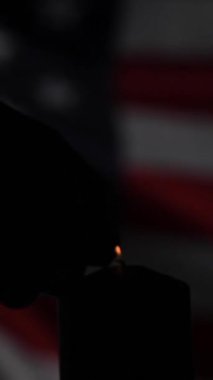 Bir adam karanlıkta Amerika Birleşik Devletleri bayrağının arka planında bir mum yakıyor. Yavaş çekim