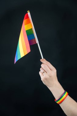 Evlilik yüzüklü kadın siyah arka planda gökkuşağı bayrağı taşıyor.