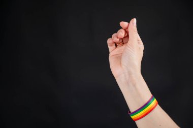 Alyansı ve gökkuşağı bileziği olan kadın siyah arka planda kalp işareti gösteriyor.