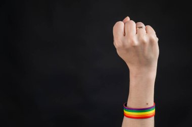 Evlilik yüzüğü ve gökkuşağı bileziği olan kadın siyah arka planda yumruğunu tutuyor.