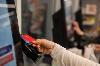 Bu resim, bir otomatik ödeme terminaline yaklaşırken kırmızı bir kredi kartı tutan bir eli yakalar.