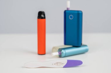 Hamilelik testi, elektronik sigara ve tek kullanımlık vazo beyaz masada.