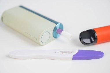 Hamilelik testi, elektronik sigara ve tek kullanımlık vazo beyaz masada.