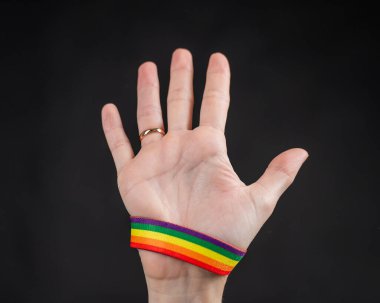 Alyansı ve gökkuşağı bileziği olan kadın siyah arka planda avuç içi tutuyor.