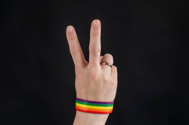 Alyansı ve gökkuşağı bileziği olan kadın siyah arka planda avuç içi tutuyor.