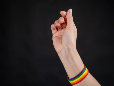 Alyansı ve gökkuşağı bileziği olan kadın siyah arka planda kalp işareti gösteriyor.