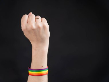 Evlilik yüzüğü ve gökkuşağı bileziği olan kadın siyah arka planda yumruğunu tutuyor.