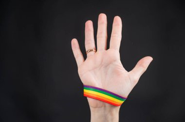 Alyansı ve gökkuşağı bileziği olan kadın siyah arka planda avuç içi tutuyor.