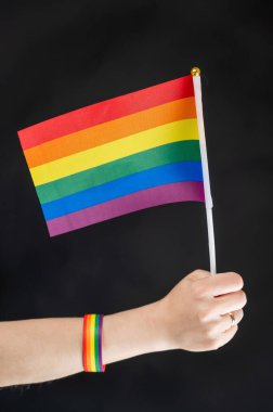 Evlilik yüzüklü kadın siyah arka planda gökkuşağı bayrağı taşıyor.