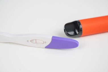 Hamilelik testi, elektronik sigara ve tek kullanımlık vazo beyaz masada.