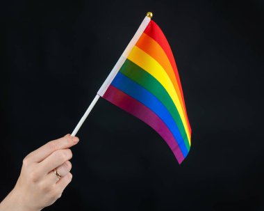 Evlilik yüzüklü kadın siyah arka planda gökkuşağı bayrağı taşıyor.