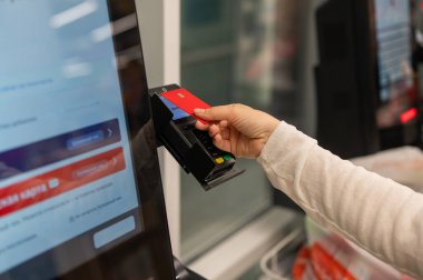 Bu resim, bir otomatik ödeme terminaline yaklaşırken kırmızı bir kredi kartı tutan bir eli yakalar.