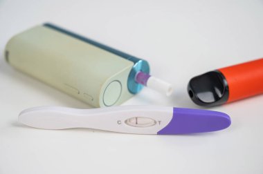 Hamilelik testi, elektronik sigara ve tek kullanımlık vazo beyaz masada.