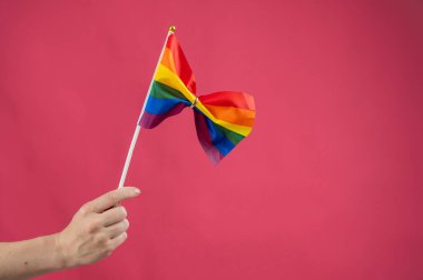 Elinde gökkuşağı bayrağı tutan kadın pembe arka planda alyansla bağlanmış.