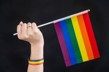 Evlilik yüzüklü kadın siyah arka planda gökkuşağı bayrağı taşıyor.