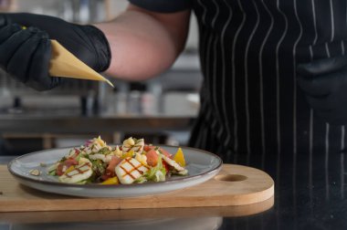 Şef salatayı sosla doldurur.