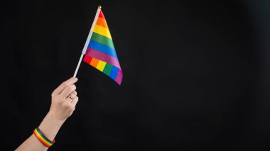 Evlilik yüzüklü kadın siyah arka planda gökkuşağı bayrağı taşıyor.