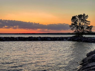 Gölün üzerinde günbatımı ön planda ağaçlarla ve arka planda kayalarla. Ontario, Kanada. 