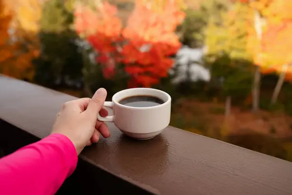 Kadın eli, sonbahar ormanında balkonda bir fincan kahve tutuyor.. 