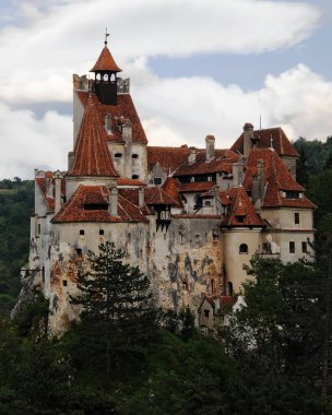 Bir Drakula 'nın şatosu, arka planda bulutlar olan ağaçların arasında, karşı tepeden (Romanya' nın Bran kentinde) görülüyor.)
