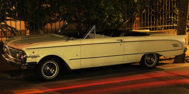 Eski bir Mercury Comet arabası kaldırım kenarına park edilmiş. Sıcak bir gece, arka planda çit. Sokaktaki diğer arabaların stop lambalarının bir işareti ve araba gövdesindeki ışıkların küçük bir yansıması (Liguria, İtalya 'da çekildi))