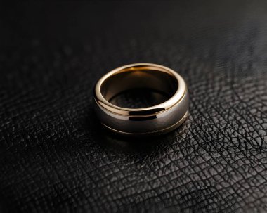 A wedding ring is positioned on a textured black surface. The ring features a sleek design with gold and silver hues, symbolizing love and commitment in a timeless fashion. clipart