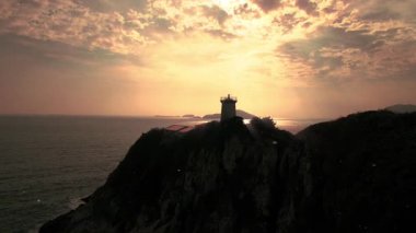 Deniz feneri silueti Rocky Sahilinde Okyanus Dalgaları Üzerinde Dramatik Günbatımına Karşı