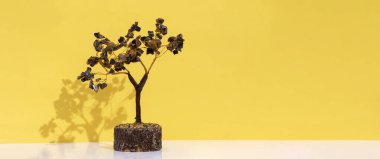 Kahverengi kristal ametist ve florür taşlı el yapımı bakır tel. Sarı duvar arkaplanında gölgesi olan ağaç.