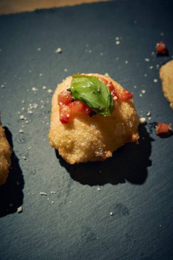 İnce dilimlenmiş taze domates ve kokulu fesleğen yapraklarıyla kaplı çıtır çıtır, altın renginde bir hamur. Bu basit ama lezzetli yemek, çıtır çıtır güveç ile taze Akdeniz lezzetini birleştirir. Aperatif ya da sokak yemeği olarak mükemmeldir..