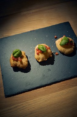 İnce dilimlenmiş taze domates ve kokulu fesleğen yapraklarıyla kaplı çıtır çıtır, altın renginde bir hamur. Bu basit ama lezzetli yemek, çıtır çıtır güveç ile taze Akdeniz lezzetini birleştirir. Aperatif ya da sokak yemeği olarak mükemmeldir..