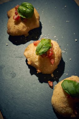 İnce dilimlenmiş taze domates ve kokulu fesleğen yapraklarıyla kaplı çıtır çıtır, altın renginde bir hamur. Bu basit ama lezzetli yemek, çıtır çıtır güveç ile taze Akdeniz lezzetini birleştirir. Aperatif ya da sokak yemeği olarak mükemmeldir..