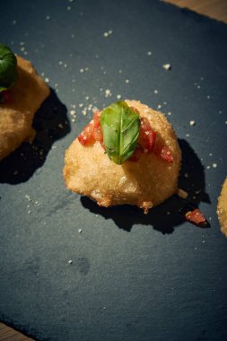 İnce dilimlenmiş taze domates ve kokulu fesleğen yapraklarıyla kaplı çıtır çıtır, altın renginde bir hamur. Bu basit ama lezzetli yemek, çıtır çıtır güveç ile taze Akdeniz lezzetini birleştirir. Aperatif ya da sokak yemeği olarak mükemmeldir..