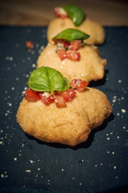 İnce dilimlenmiş taze domates ve kokulu fesleğen yapraklarıyla kaplı çıtır çıtır, altın renginde bir hamur. Bu basit ama lezzetli yemek, çıtır çıtır güveç ile taze Akdeniz lezzetini birleştirir. Aperatif ya da sokak yemeği olarak mükemmeldir..
