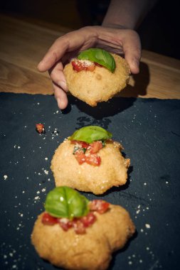 İnce dilimlenmiş taze domates ve kokulu fesleğen yapraklarıyla kaplı çıtır çıtır, altın renginde bir hamur. Bu basit ama lezzetli yemek, çıtır çıtır güveç ile taze Akdeniz lezzetini birleştirir. Aperatif ya da sokak yemeği olarak mükemmeldir..