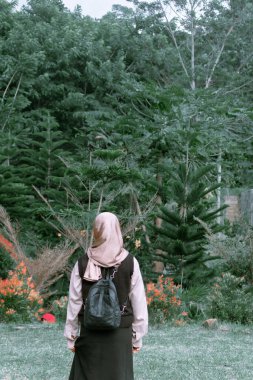 Uzun ağaçlar ve renkli çiçeklerle çevrili yeşil bir ormanda dikilen bir insanın sakin bir görüntüsü..