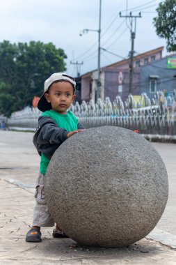 Küçük çocuk şehirde taşın üstünde oynuyor.