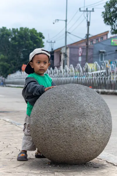 Küçük çocuk şehirde taşın üstünde oynuyor.