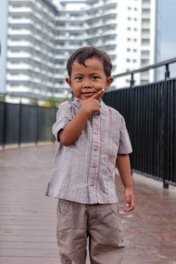 Neşeli bir çocuk, arka planında modern bir gökdelen olan yaya köprüsünde güvenli bir şekilde poz vererek, kentsel ve eğlenceli bir sahne yaratıyor.